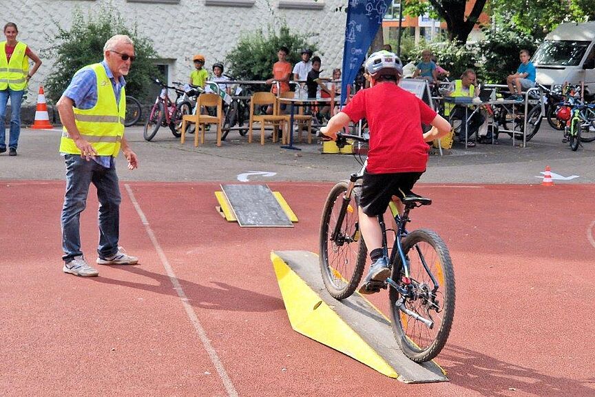 Geschicklichkeitsradfahren_ADFCAalen.jpeg Eines der Hindernisse beim Geschicklichkeitsradfahren in Aalen: Ein Kind fährt über eine Wippe. Ein ADFC-Mitglied gibt Hilfestellung.