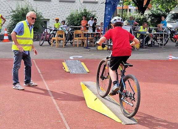 Eines der Hindernisse beim Geschicklichkeitsradfahren in Aalen: Ein Kind fährt über eine Wippe. Ein ADFC-Mitglied gibt Hilfestellung.