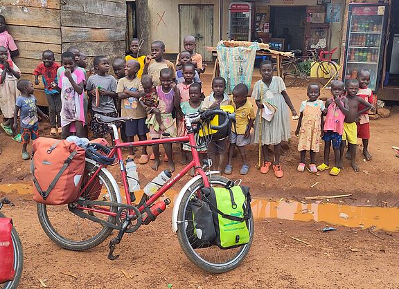 Radtour durch Ostafrika, viele Kinder stehen am Straßenrand vor einem afrikanischen Geschäft und bestaunen die ihnen fremden Männer mit den Fahrrädern