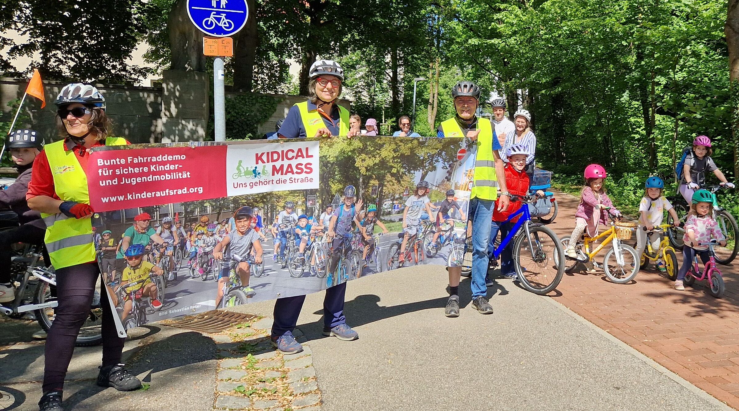 Am Start Kidical Mass 2025, drei Radfahrerinnen heben das Banner ins Bild
