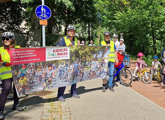 Am Start Kidical Mass 2025, drei Radfahrerinnen heben das Banner ins Bild